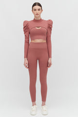 Woman in a long-sleeve crop top and leggings, standing straight facing forward.