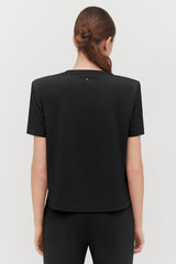 Person standing with back to the camera, wearing a t-shirt and hair tied in a bun.