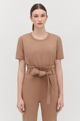 Woman in a belted jumpsuit standing against a plain background.