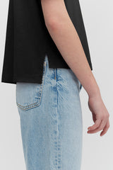 Person standing with hand resting on hip, partial view showing shirt and jeans.