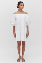 Woman in off-shoulder dress and sandals standing against a white background.