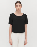 Woman standing with a plain top and trousers, looking at the camera.