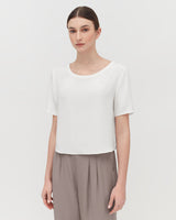 Woman wearing a blouse and pants stands facing the camera.