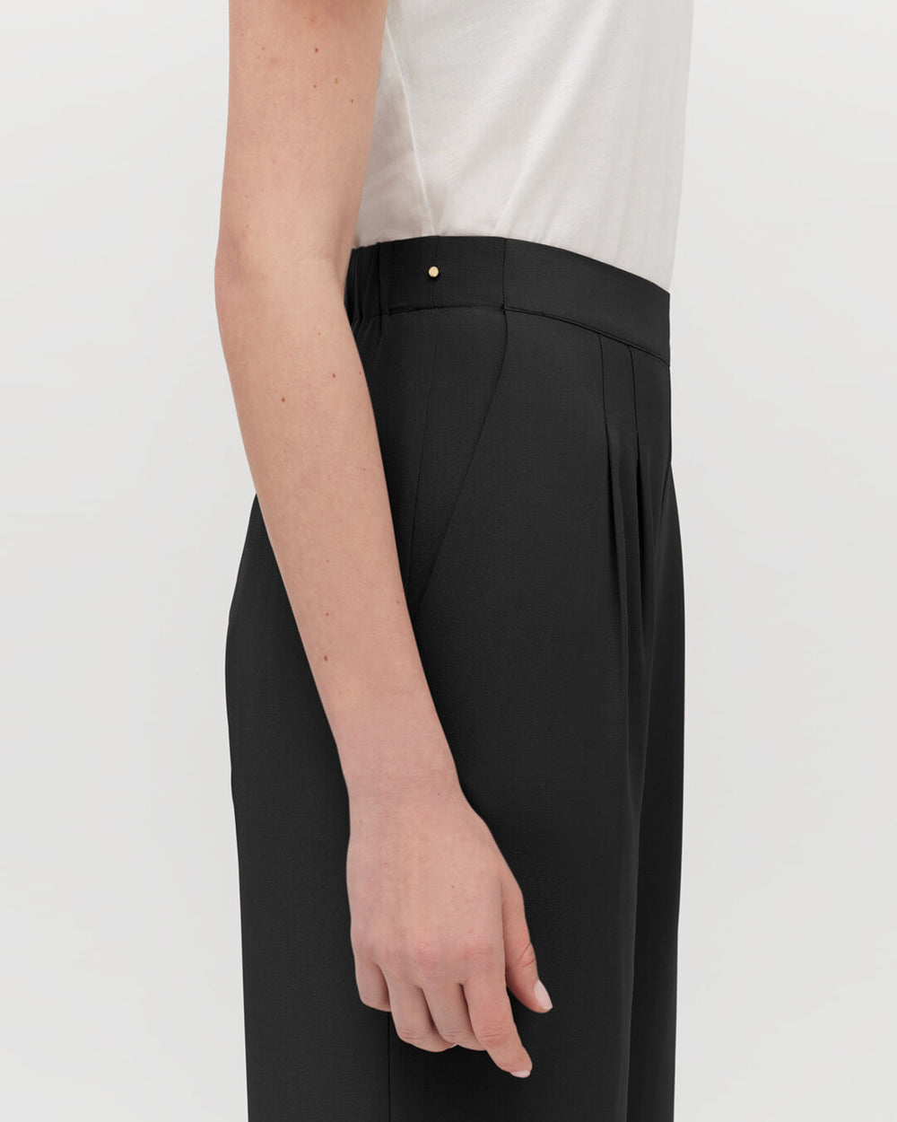 Person standing with arm at side, displaying pleated trousers.