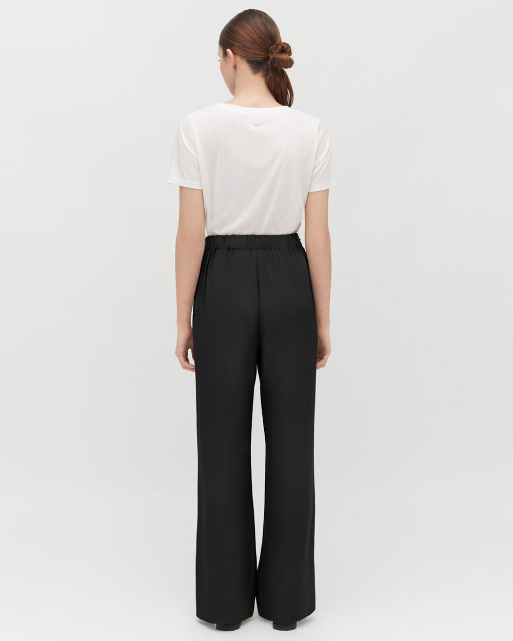 Woman standing with her back to the camera, wearing a t-shirt and pants.