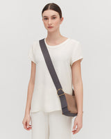 Woman standing with a crossbody bag, looking at the camera.