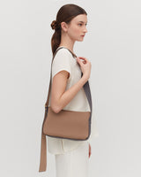 Woman standing, carrying a shoulder bag, looking to the side.