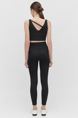 Woman facing away wearing a top with crossed back straps and leggings.