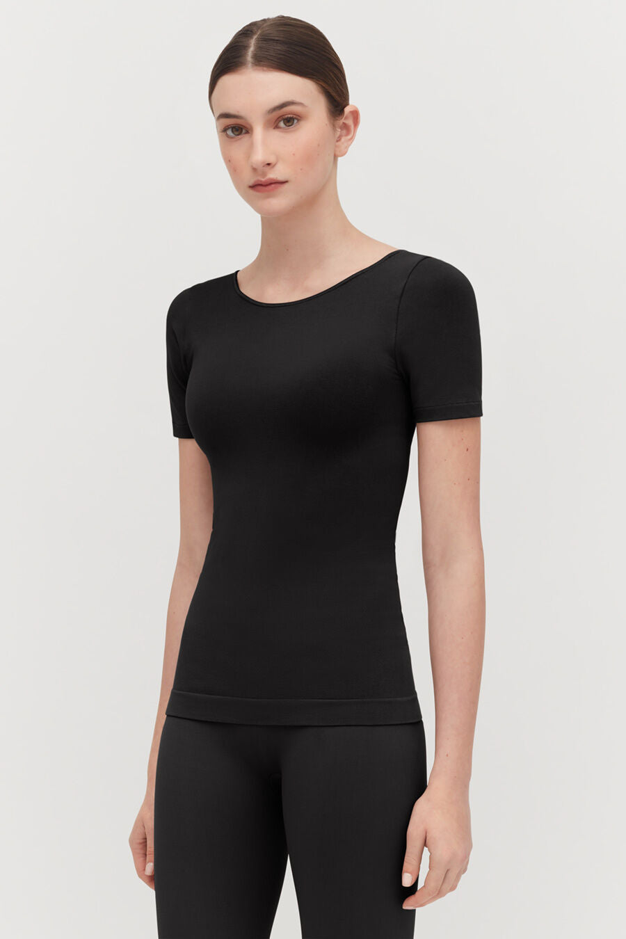Stretch Scoop Neck Tee Woman standing in a studio wearing a fitted top and leggings.