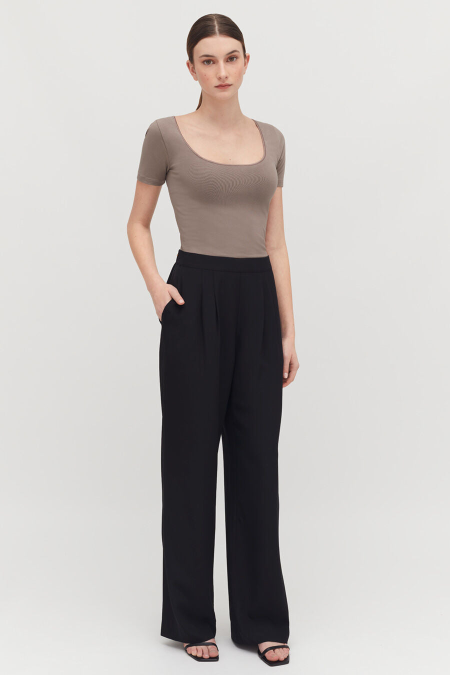 Stretch Scoop Neck Tee Woman standing in a fitted top and loose pants, hands on hips.
