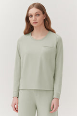 Woman in a crew neck sweatshirt with chest pocket standing in front of a plain background.