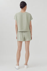 Woman in a short-sleeved top and shorts, standing with her back to the camera.