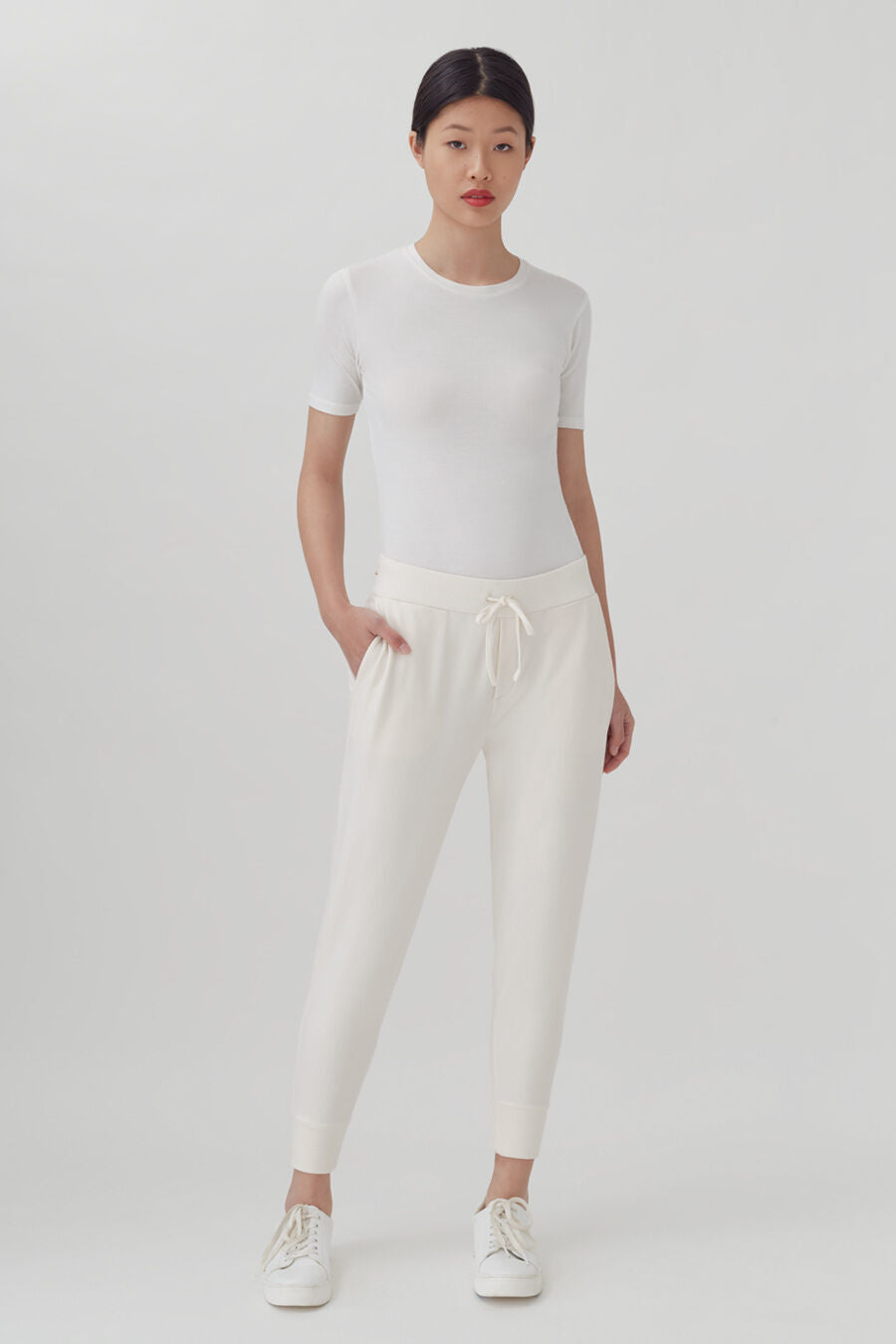 French Terry Tapered Lounge Pant Woman standing in a plain t-shirt and drawstring pants with hands on her hips.