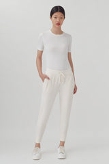 Woman standing in a plain t-shirt and drawstring pants with hands on her hips.