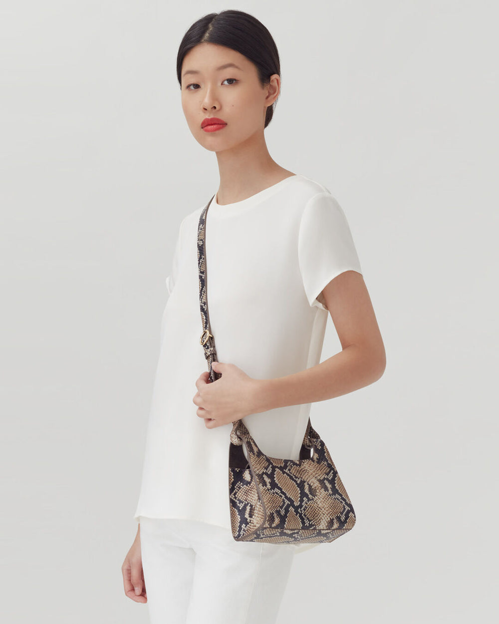 Woman standing with a crossbody bag, looking at the camera.