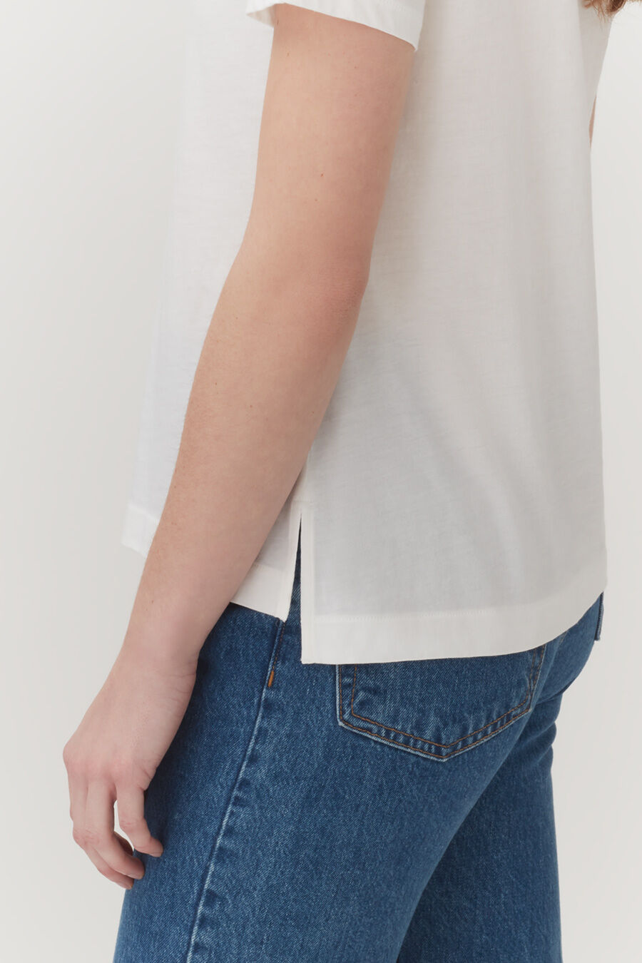 Person standing in a white top and jeans, partial view.