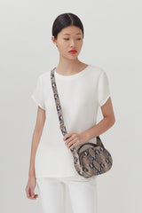 Woman standing wearing a top, pants, and crossbody bag.