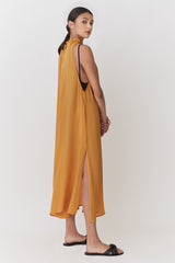 Woman in a sleeveless dress and sandals standing side view, hair in a bun.