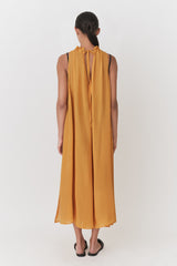 Woman in a sleeveless long dress with a tie at the neck, viewed from the back.