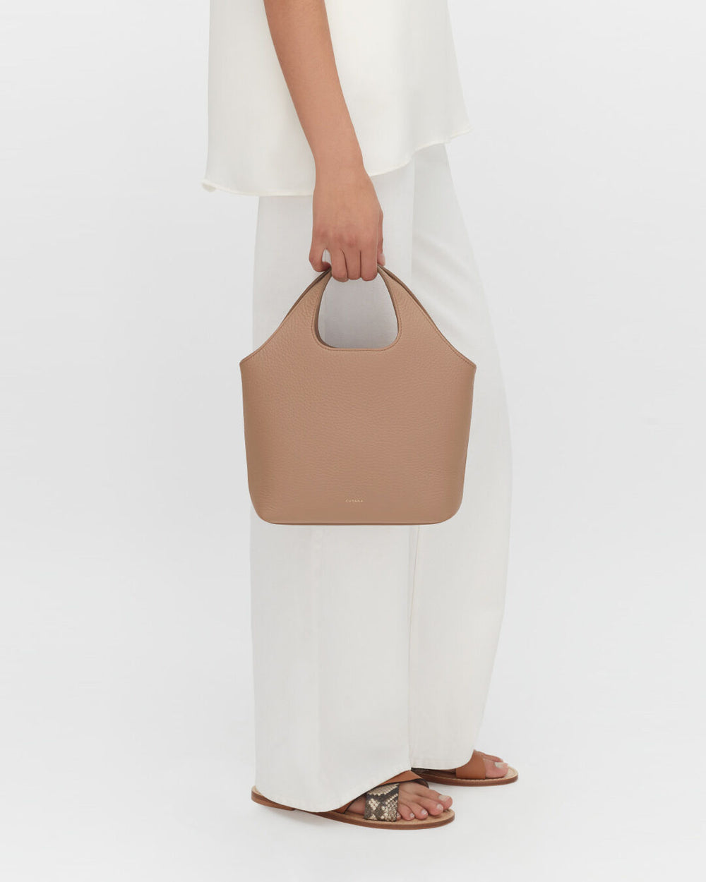 Person holding a handbag, wearing wide pants and sandals, viewed from the waist down.