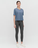 Woman standing in a studio wearing a t-shirt, leggings, and sneakers.