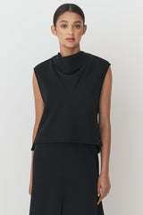 Woman in a sleeveless top and trousers standing facing the camera.