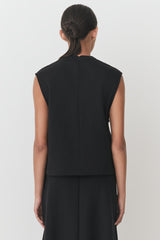 Woman viewed from behind with hair up in bun and wearing a sleeveless top and skirt.