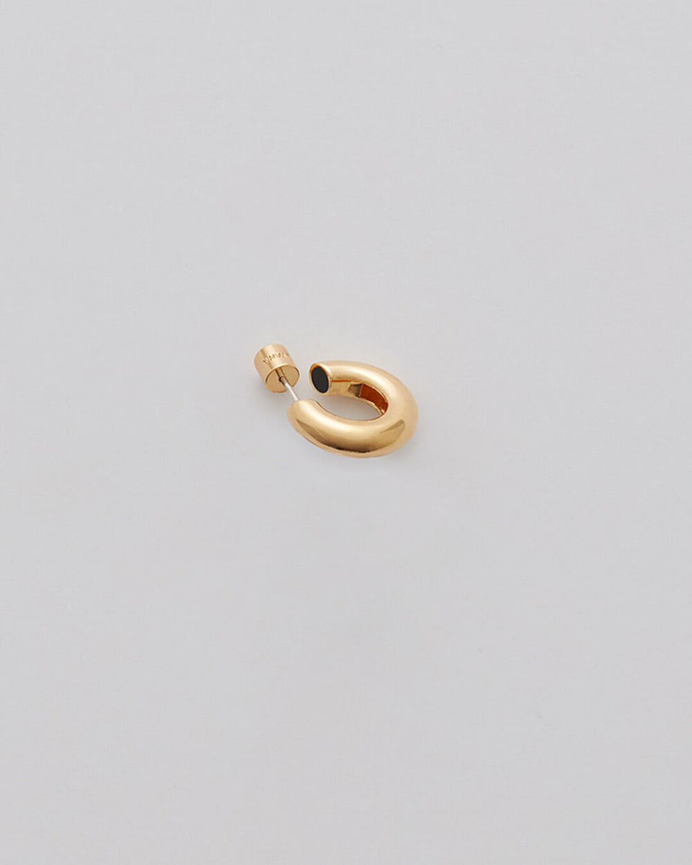 Earring in the shape of an abstract figure on a light background.