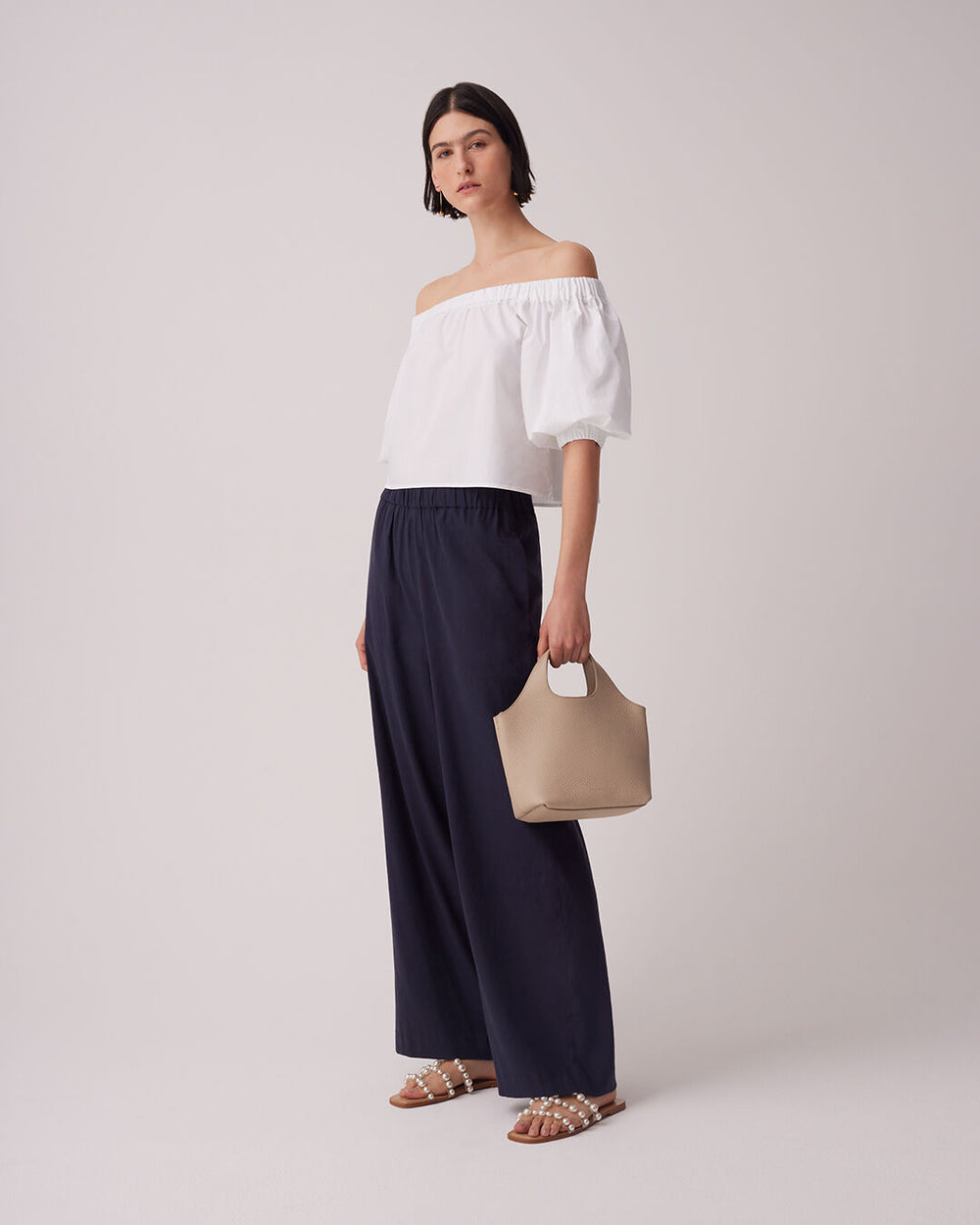 Poplin Off-The-Shoulder Cropped Top Woman standing in off-shoulder top, wide pants, holding a bag.