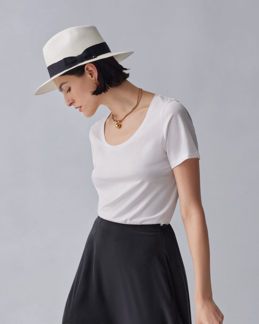 Woman wearing a hat, T-shirt, and skirt, facing sideways.