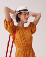 Woman in a dress and hat holding her arms up near her head.
