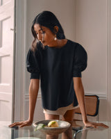 Woman leaning over a glass table with fruit on it.