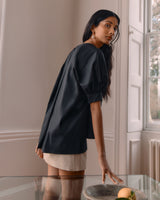 Woman standing by a table with fruit, looking over her shoulder.