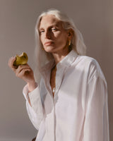 Woman holding a pear, looking contemplative.