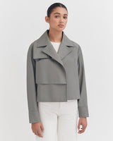 Woman in a jacket standing against a plain background.