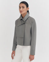 Woman in a jacket and pants standing against a plain background.