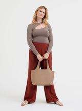 Woman standing with a handbag and wearing a long-sleeve top and wide-leg pants.