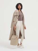 Woman standing with coat draped on shoulders, holding a handbag.