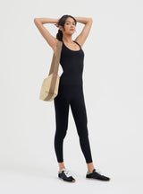 Woman standing with hands on head, carrying a shoulder bag, wearing athletic outfit and sneakers.