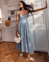 Woman in a dress standing in a room with hand raised.