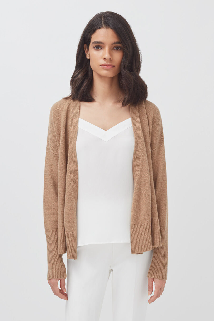 Woman standing in a cardigan over a top with plain background.