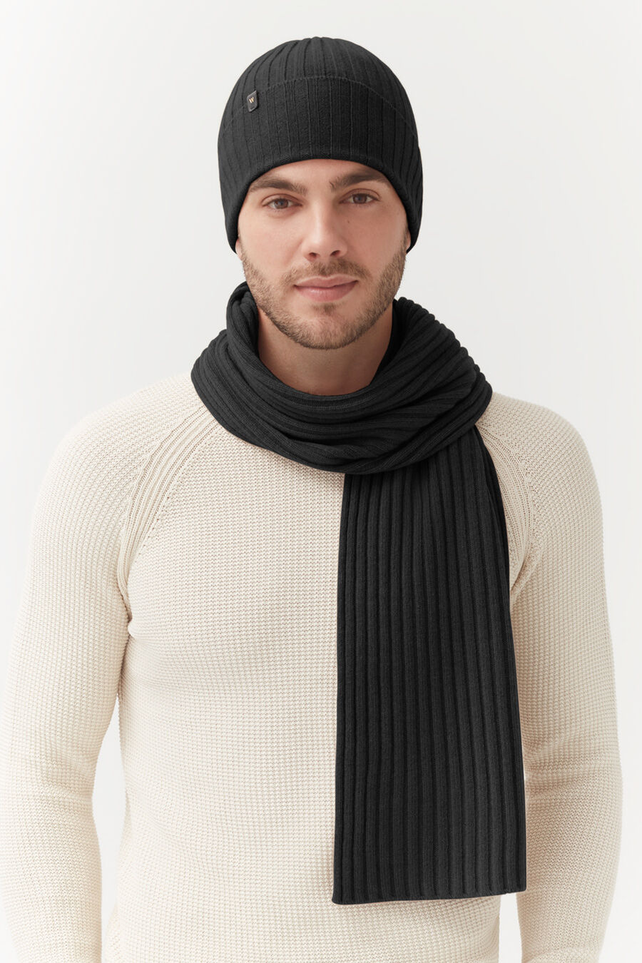 Man wearing a beanie and scarf, standing indoors.
