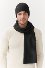 Man wearing a beanie and scarf, standing indoors.