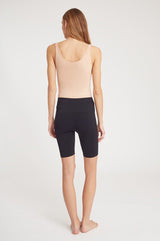 Person seen from behind, wearing a sleeveless top and knee-length shorts, standing barefoot.