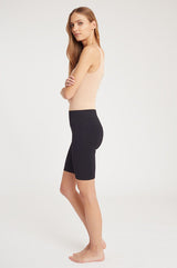 Woman standing side-on, wearing a tank top and shorts, looking over her shoulder.