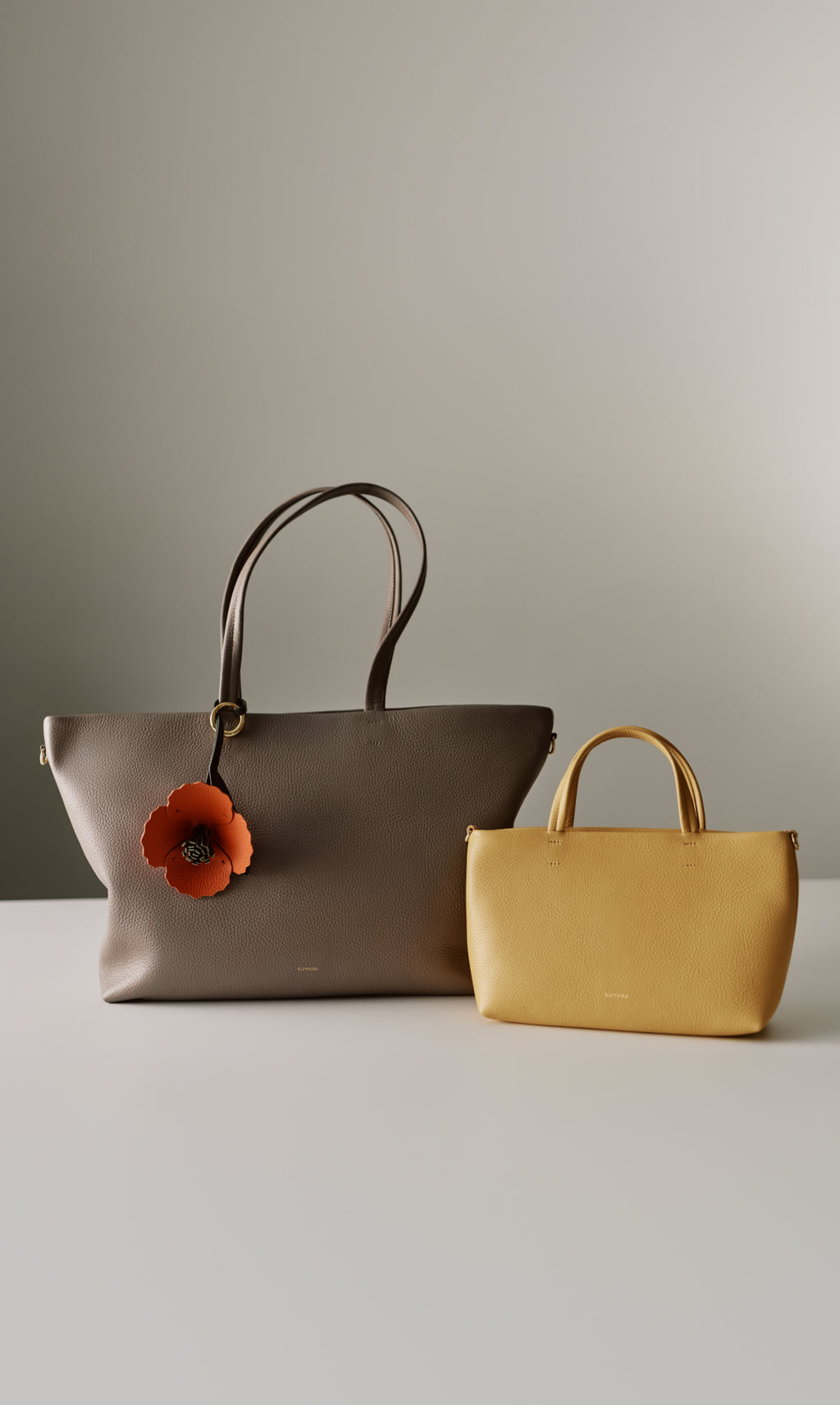 Two handbags on a surface, one with a flower charm.