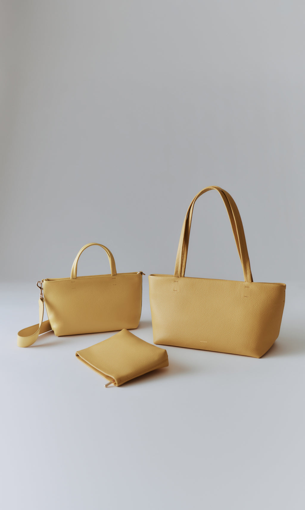 Three handbags on a plain background, one with long straps.