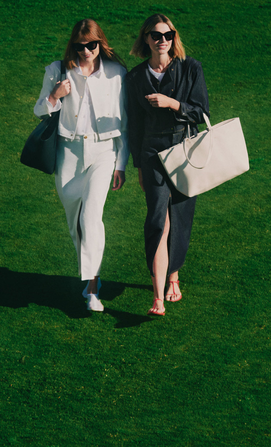 Two people walking on grass, each carrying a large bag and wearing sunglasses.