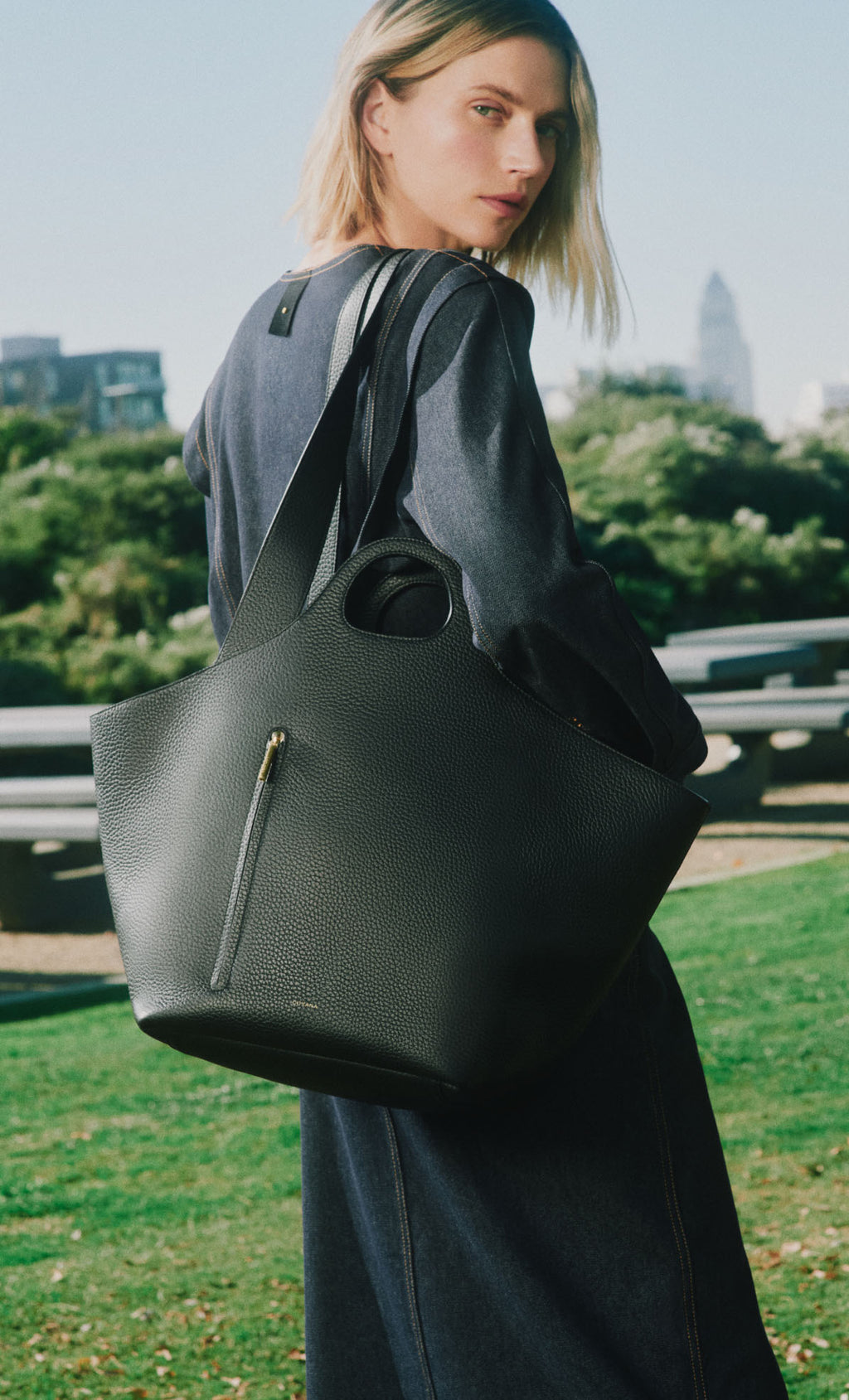 Person outdoors holding a large bag, city skyline in background.