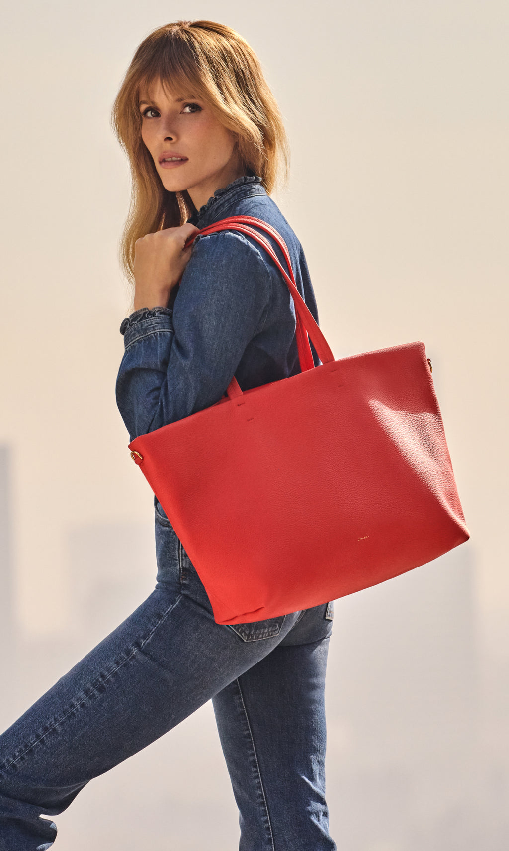Person holding a large bag and wearing a denim outfit in an outdoor setting.